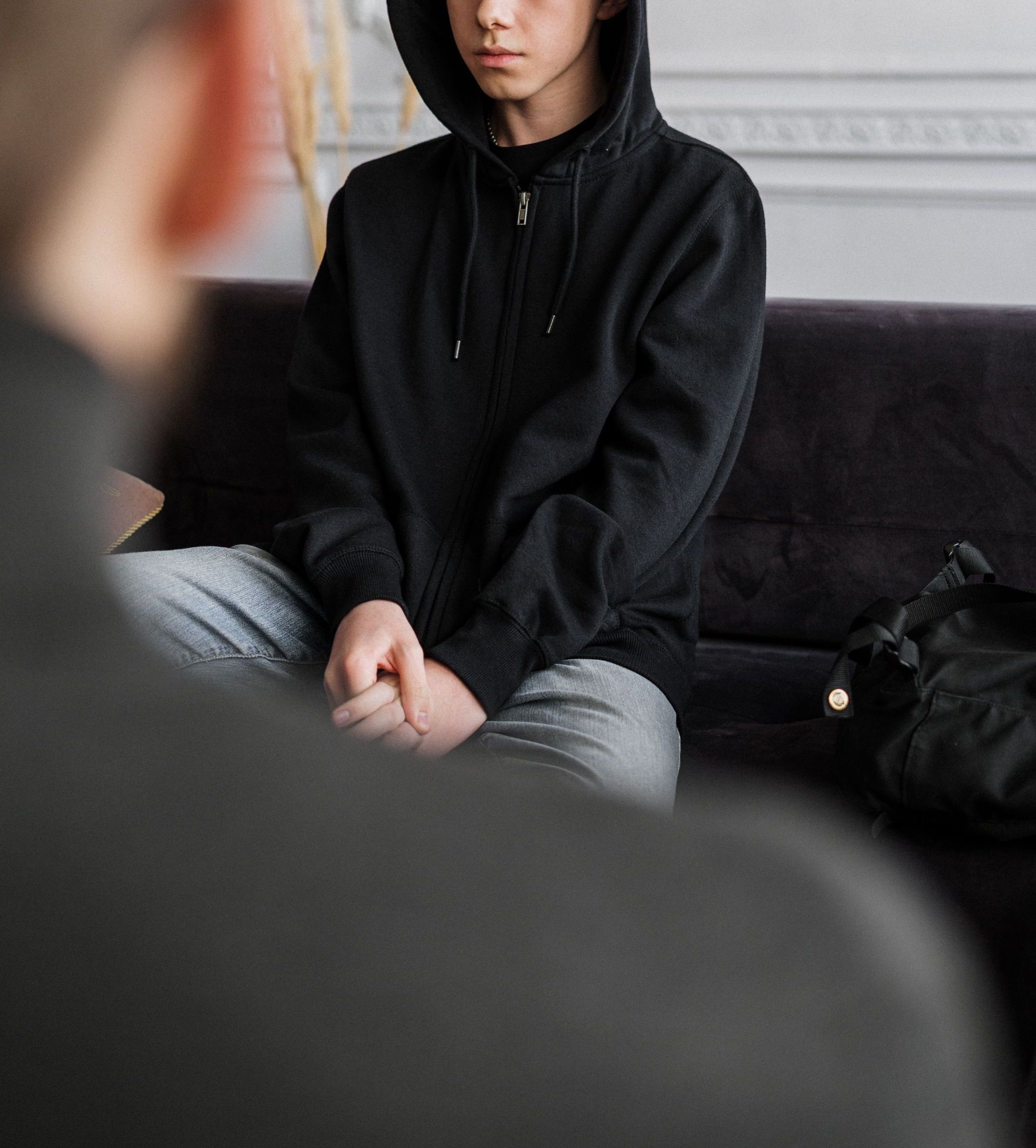 A teenager in a black hoodie engages in a counseling session, sitting calmly indoors.