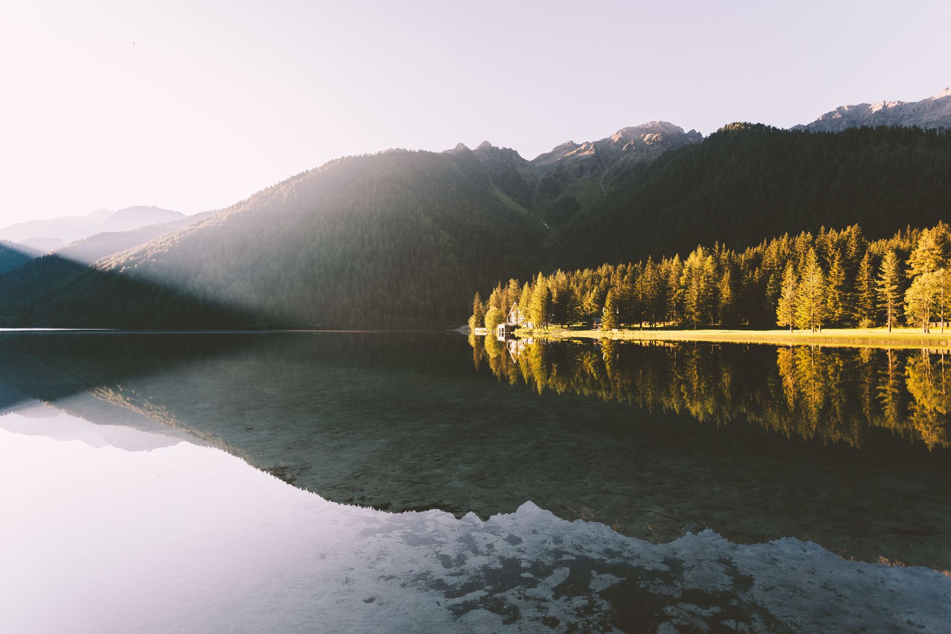 A tranquil view of a mountain and forest reflected in a calm lake at dawn.